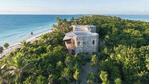 A beachfront property surrounded by dense tropical vegetation, featuring a stone building with multiple rooms and a visible balcony. - ANANA Casa Kaab Kaan (Tulum)