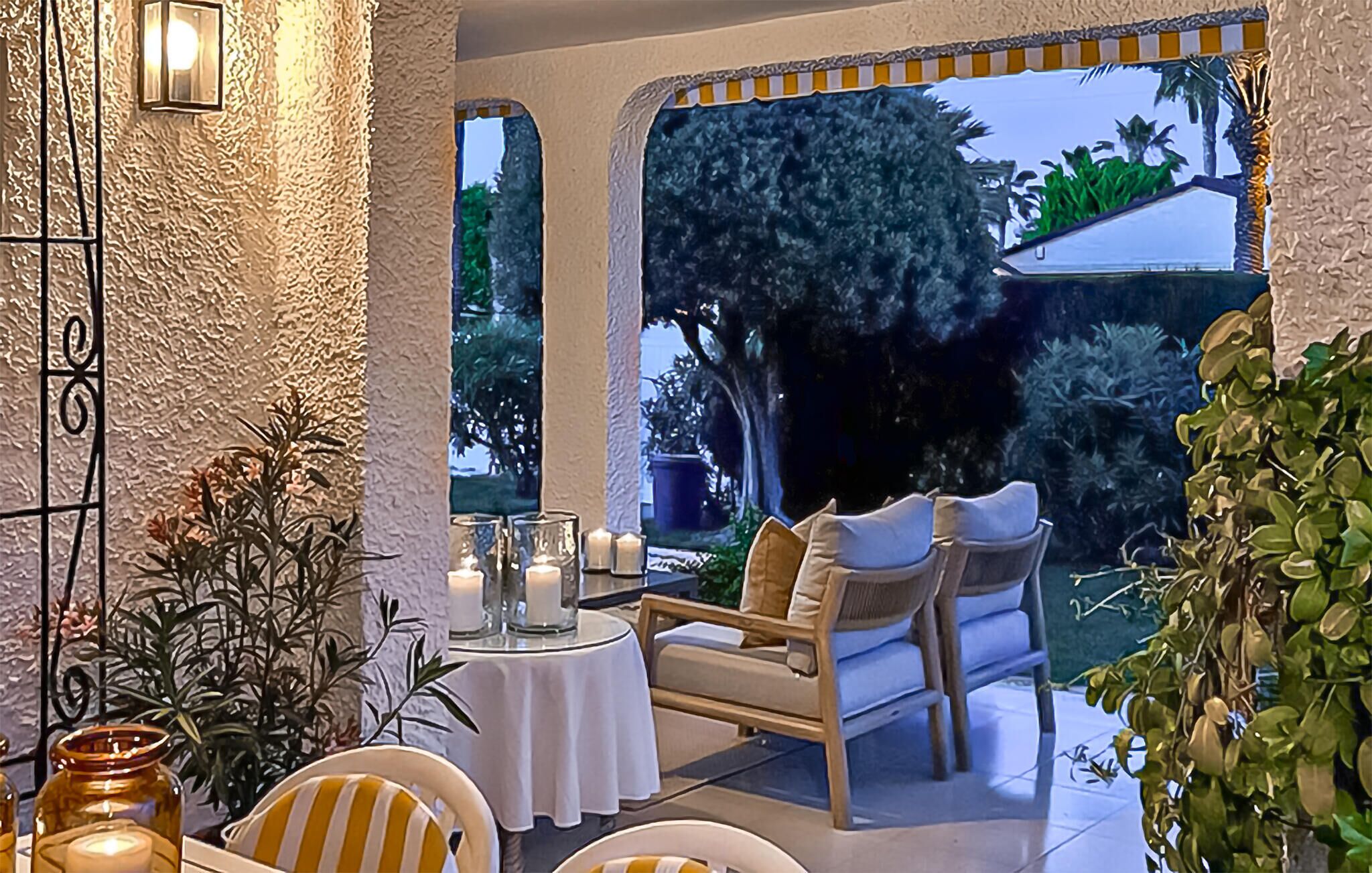 A cozy outdoor seating area with a table and chairs, surrounded by plants and a view of a garden.