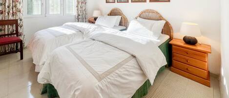 A double bed with white bedding, a wooden nightstand with a lamp, and a green chair.