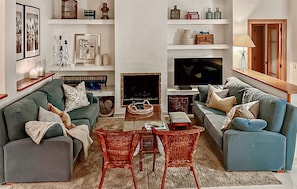 Un salon avec deux canapés, une table basse et un téléviseur. On y trouve des étagères ornées d’objets décoratifs et une cheminée.