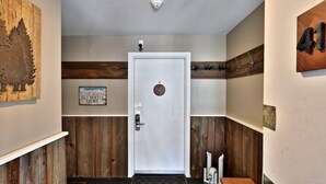 A hallway with a white door marked with the number 413, a sign requesting removal of ski boots, and a coat rack with hangers.