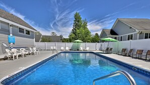 A rectangular swimming pool with a blue tile border, surrounded by white lounge chairs and umbrellas.