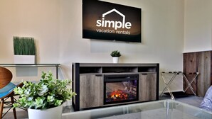 A modern living room with a fireplace, a mounted TV displaying 'simple vacation rentals', and a glass coffee table.