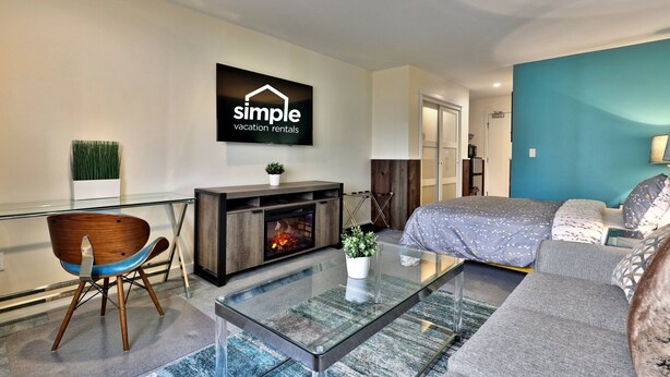 A modern living room with a glass coffee table, a sofa, a TV mounted on the wall, a fireplace, and a blue accent wall.