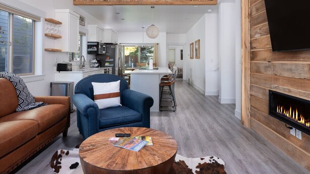 A spacious living area with a high ceiling, a fireplace, and a kitchen in the background. - Modern Victor Townhome | Walk to Town (Victor)