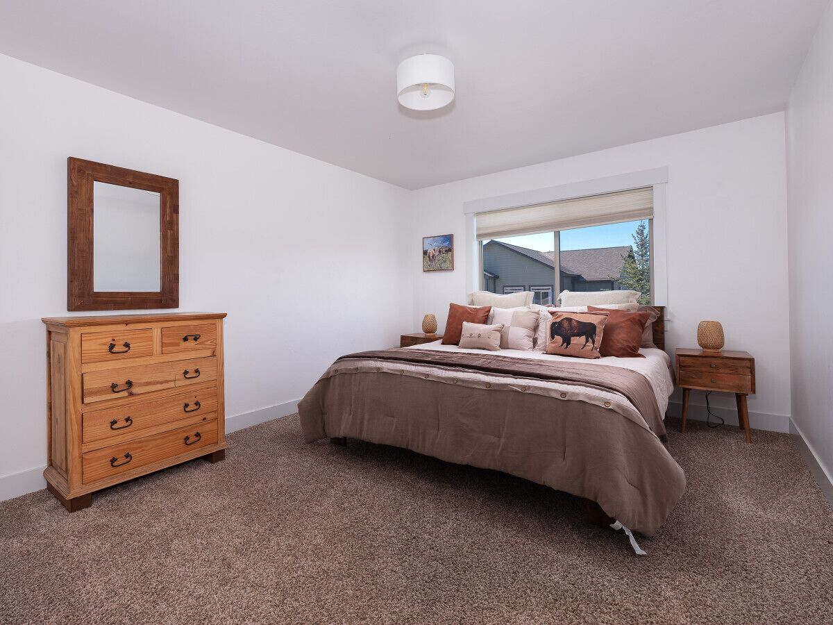 Un dormitorio con cama, cómoda de madera, ventana y una lámpara en el techo.