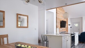 A modern kitchen with white cabinets, a wooden island, and a dining table with a metal tray. - Modern Victor Townhome | Walk to Town (Victor)