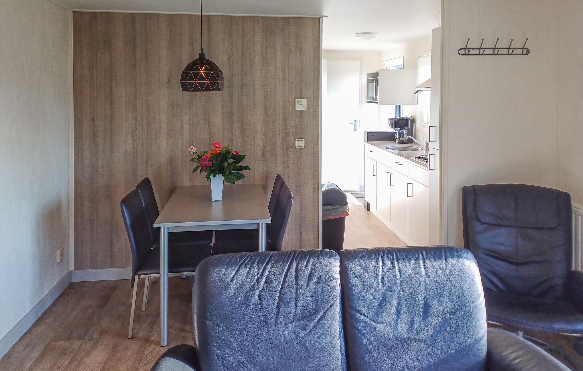Ein moderner Essbereich mit einer Wandpaneele aus Holz, einer hängenden Pendelleuchte und einem Tisch mit Stühlen. Im Hintergrund ist ein Mülleimer zu sehen.