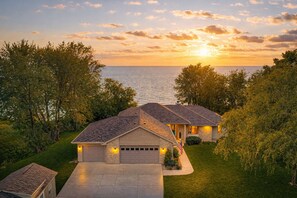 Una casa a due piani con garage, vialetto e vista sull'oceano al tramonto.