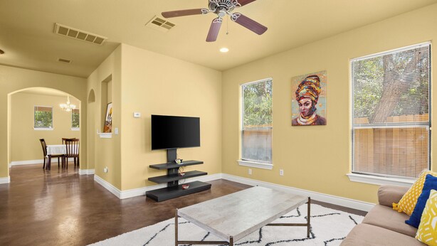 A living room with a flat-screen TV, a ceiling fan, a dining area with a table and chairs, and artwork on the walls.