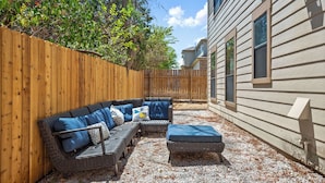 A backyard with a wooden fence, a wicker sofa with cushions, and a small table.
