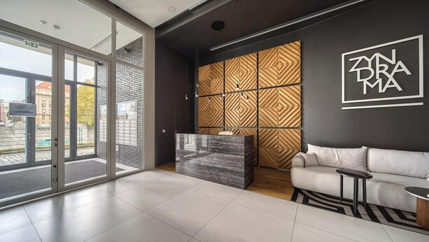 Ein modernes Interieur mit einer großen Glastür, die zu einem Außenbereich führt, einem Empfangsbereich, einer Wand mit Muster und einem Sofa.