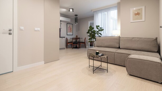 A modern living room with a beige sofa, a coffee table, and a dining area with a table and chairs. - Chopina Glamour Apartment (Katowice)