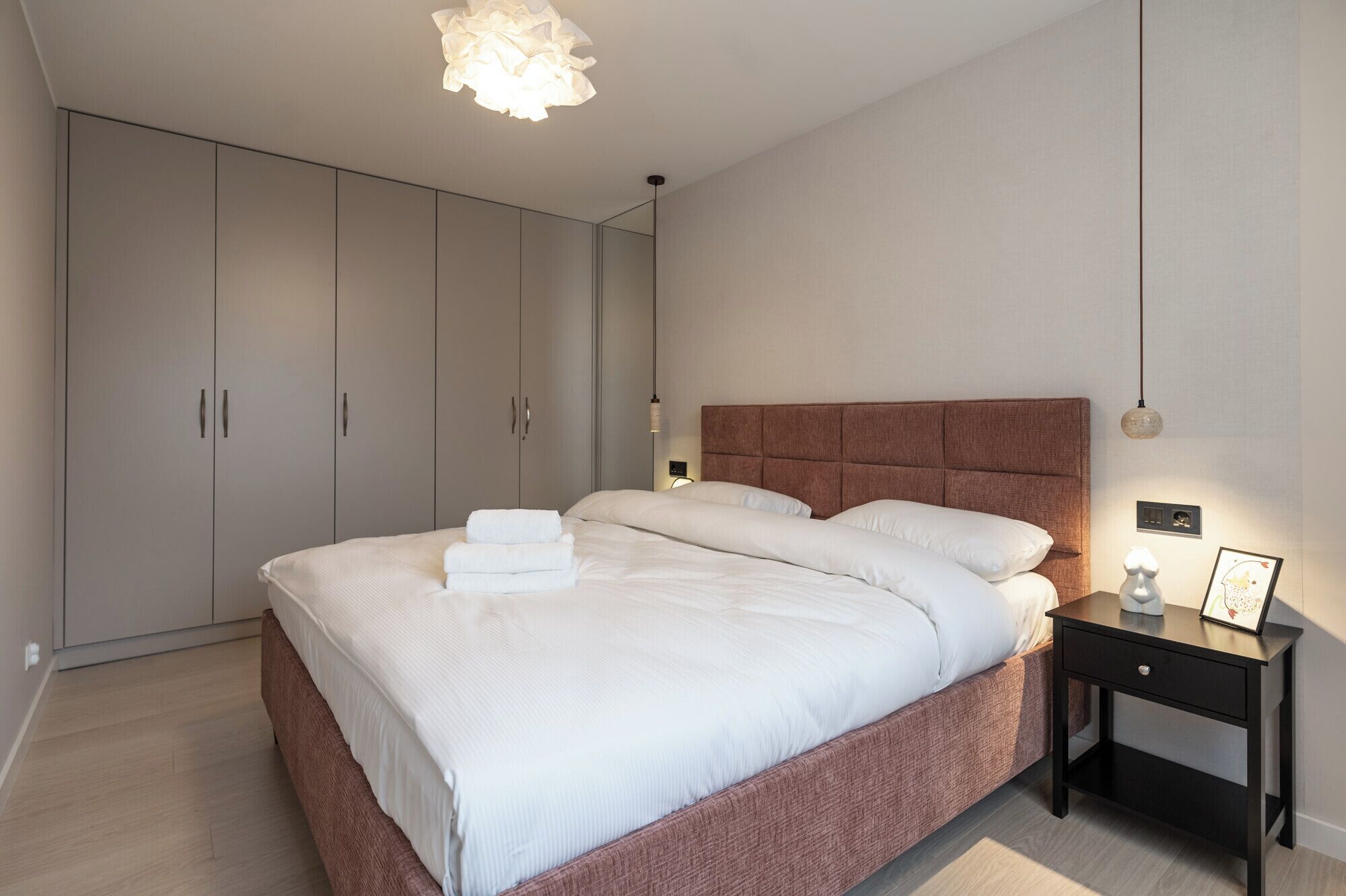 A bedroom with a large bed, a nightstand, a wardrobe, and a hanging light fixture.