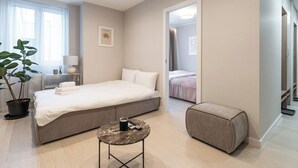 A modern hotel room with a large bed, a bedside table with a lamp, a potted plant, and a small ottoman. - Chopina Glamour Apartment (Katowice)