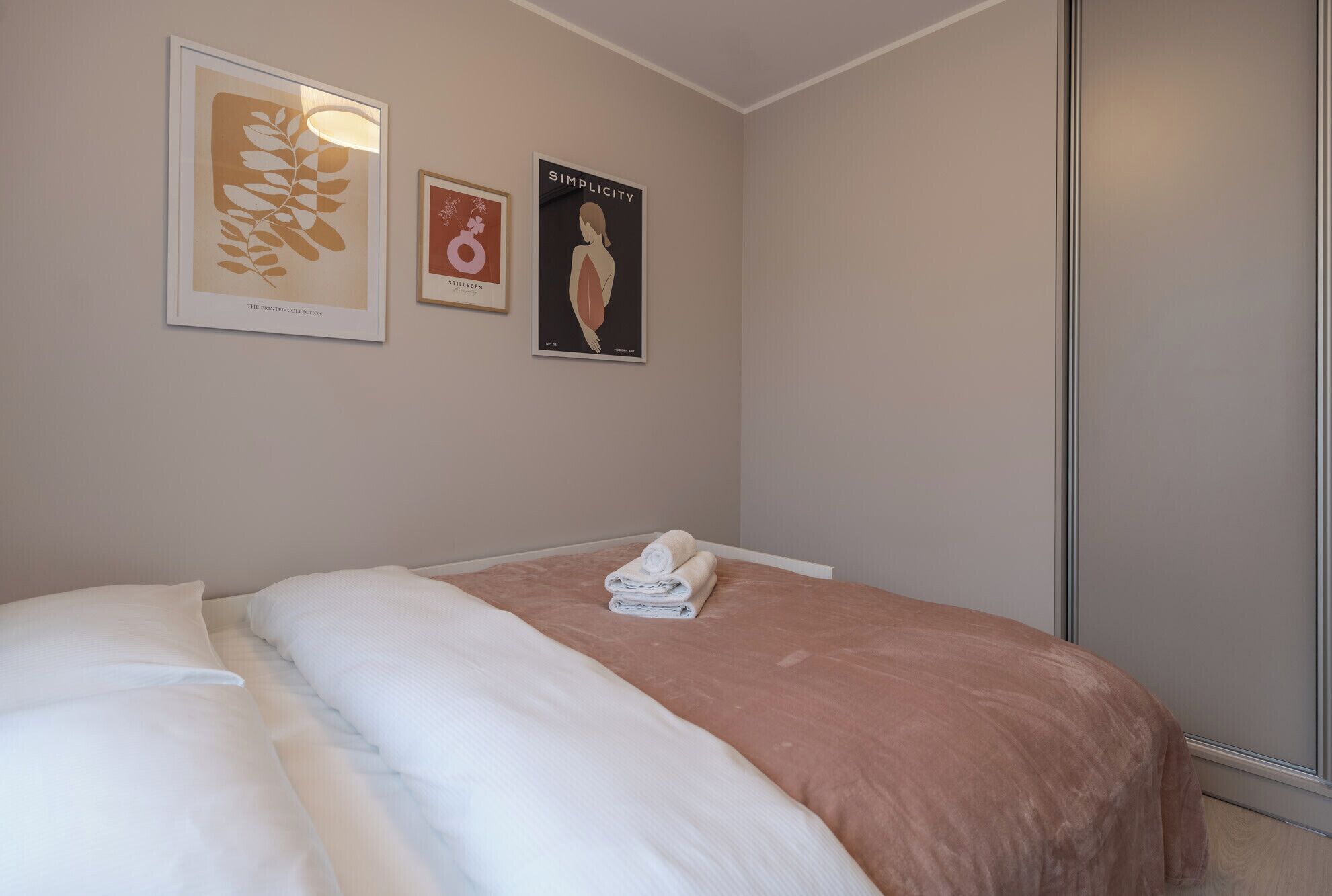 Un dormitorio con cama, mesita de noche y tres cuadros en la pared.