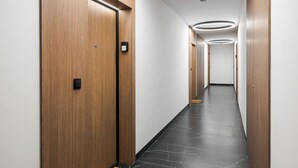 Un pasillo moderno de hotel con puertas de madera, suelo de mármol negro e iluminación empotrada.