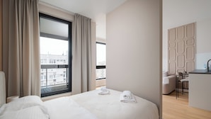 Habitación de hotel moderna con una cama grande, un escritorio con una silla y vistas de la ciudad a través de un ventanal.