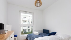 Un dormitorio con cama, escritorio, silla y ventana con vista a edificios.