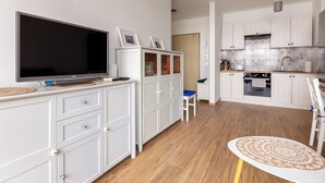 Una cocina moderna con armarios blancos, un televisor de pantalla plana grande y una zona de comedor con una mesa redonda.