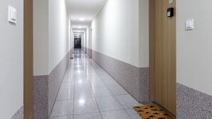 Un largo pasillo bien iluminado, con una puerta de madera que tiene el número 89, que da a una habitación.