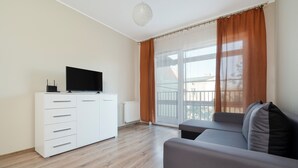A modern living room with a white cabinet, a flat-screen TV, a grey sofa, and a large window with curtains. - Pogonowskiego 2-Bedroom Apartment (Lódz)