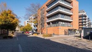 A modern building with a brick facade, multiple balconies, and a parking area with cars. - Pogonowskiego 2-Bedroom Apartment (Lódz)