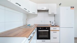 A modern kitchen with white cabinetry, a wooden countertop, a built-in oven, and a white refrigerator. - Pogonowskiego 2-Bedroom Apartment (Lódz)