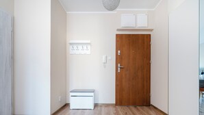 A hallway with a wooden door, a small bench, a coat rack, and a wall-mounted phone. - Pogonowskiego 2-Bedroom Apartment (Lódz)