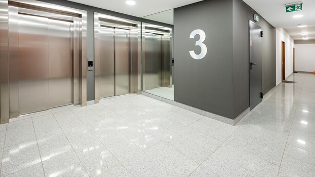 A modern elevator area with a large number '3' sign, a clean tiled floor, and a plain wall. - Pogonowskiego 2-Bedroom Apartment (Lódz)