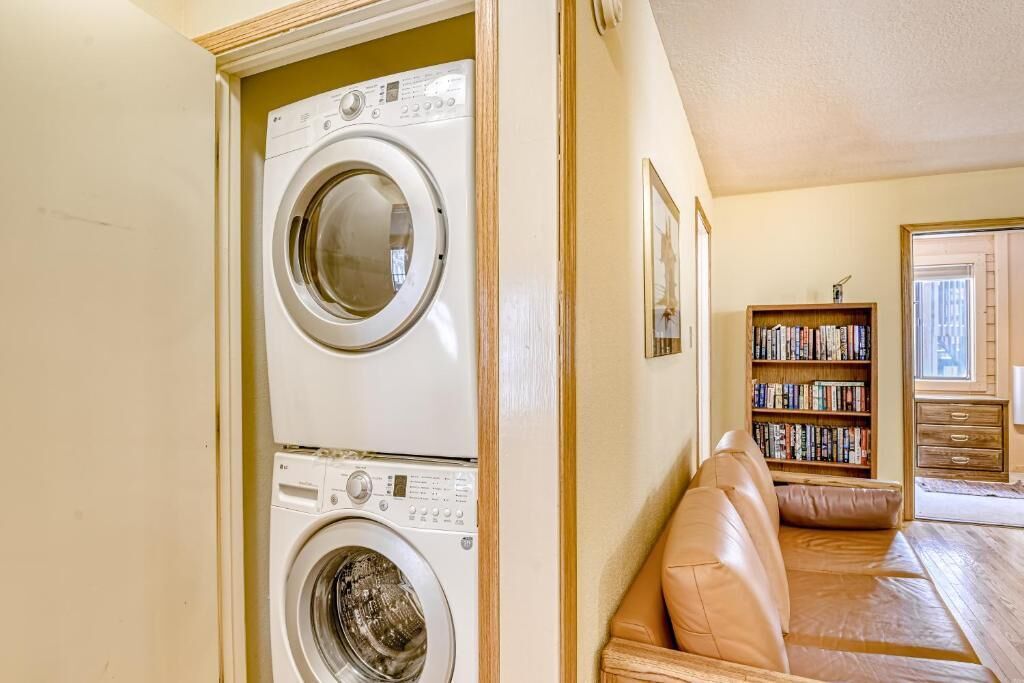 A laundry room with two stacked washing machines, a bookshelf with books, and a leather sofa.