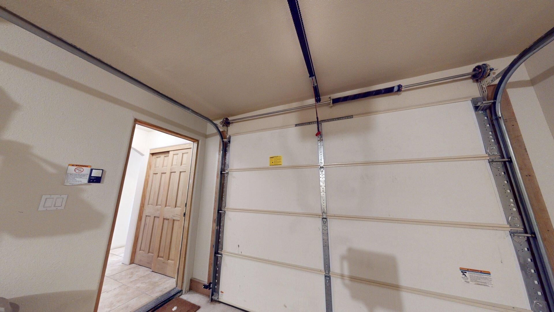 Un garage avec une porte métallique fermée, une porte en bois donnant sur une autre pièce et un paillasson sur le sol.