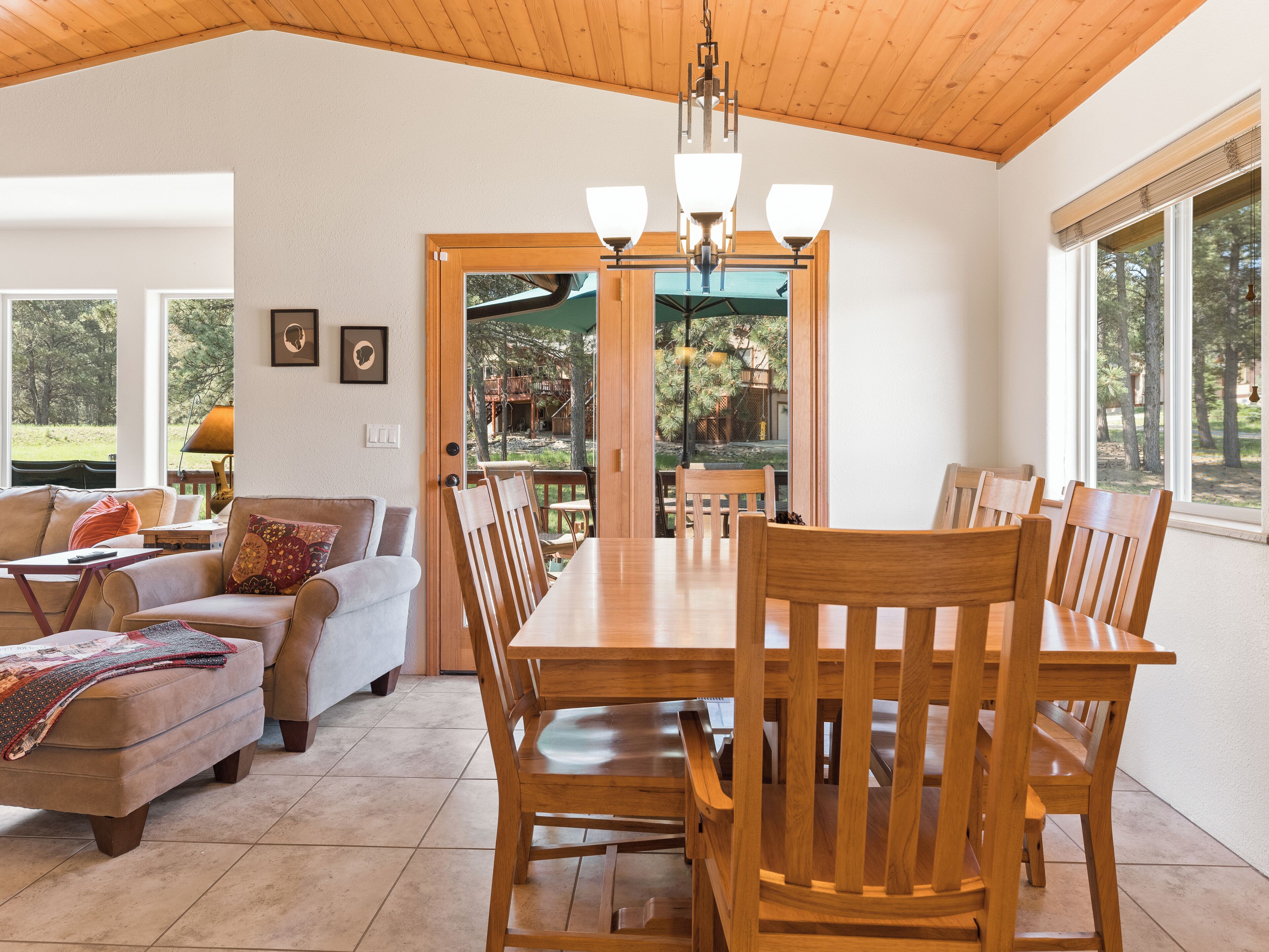 Un amplio comedor con una mesa y sillas de madera, un sofá y vistas a una terraza y árboles.