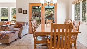 A spacious dining area with a wooden table and chairs, a sofa, and a view of a deck and trees. - Convenient Location | Fireplace | Pet Friendly | Country Club Villas 13 (Angel Fire)