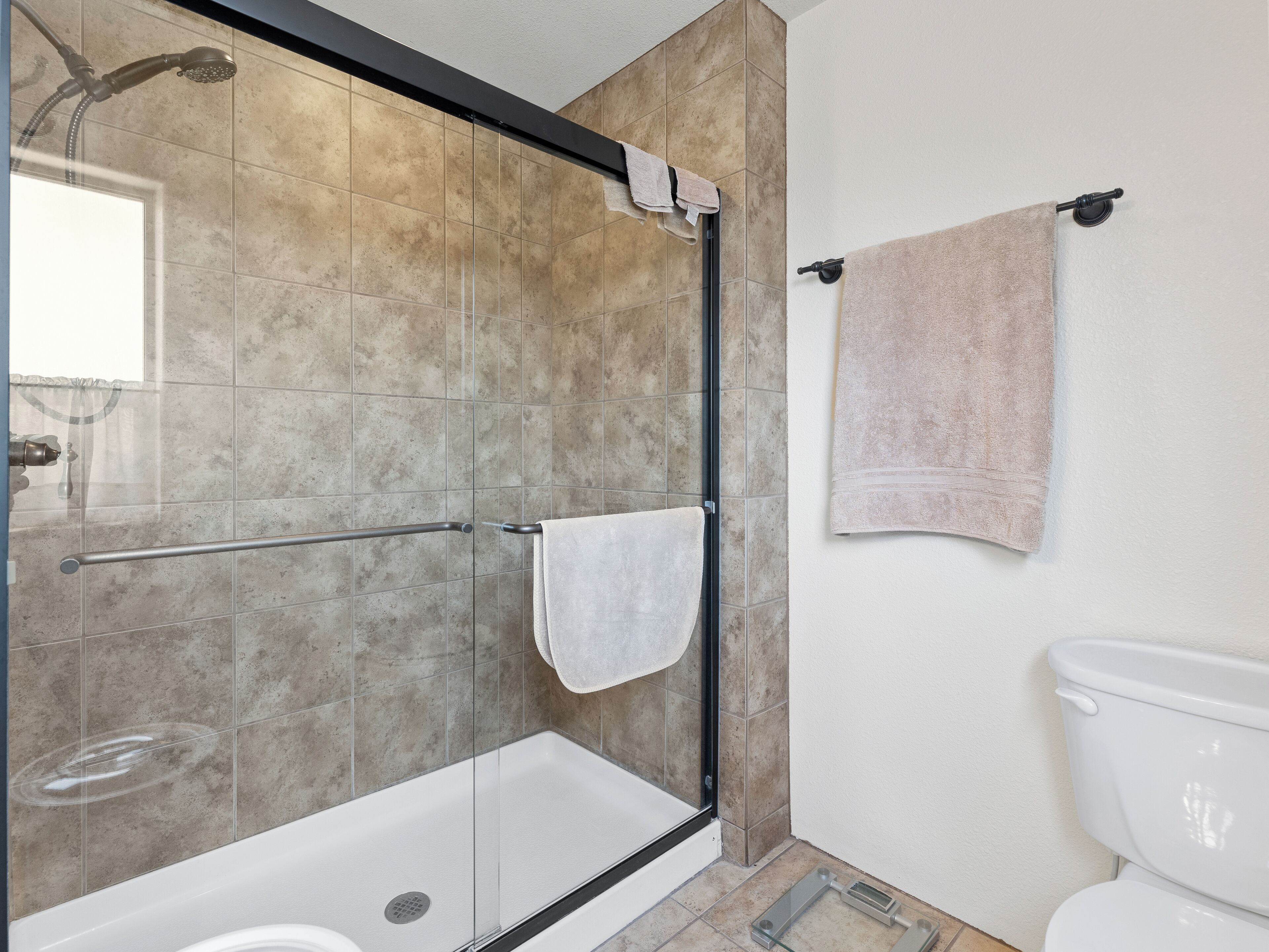 A modern bathroom with a glass-enclosed shower, a white toilet, and beige tiles.