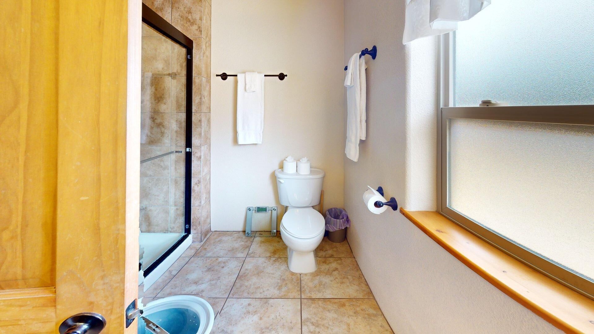 Et lille badeværelse med toilet, brusebad og et vindue.