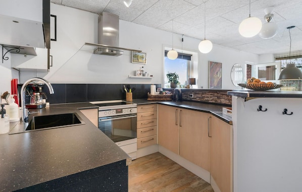 Una cocina moderna con horno empotrado, un lavamanos y una isla grande. Hay armarios de madera y una ventana que proporciona luz natural.
