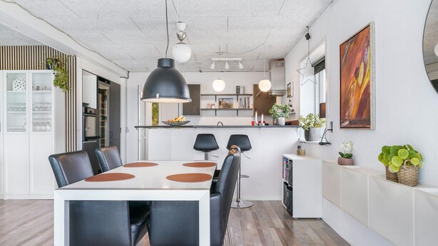 Una cocina moderna con una isla central, iluminación colgante y un comedor con mesa blanca y sillas negras.