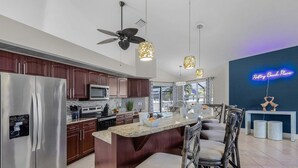 Une cuisine moderne dotée d’un îlot central, d’appareils électroménagers en acier inoxydable et de luminaires suspendus.