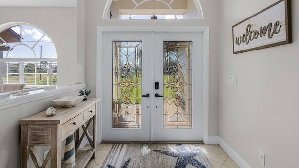 Un hall d’entrée doté d’une porte à deux battants ornée de vitraux, d’une enseigne « Bienvenue », d’une console et d’un banc.