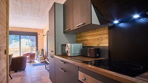 A compact kitchen with wooden cabinetry, a built-in microwave, a stove, and a view of the outdoors through a sliding door. - Chalet du Souillet with Mountain Views, Private Terrace and Wi-Fi (Saint-Pierre-d'Entremont)