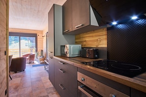 A compact kitchen with wooden cabinetry, a built-in microwave, a stove, and a view of the outdoors through a sliding door. - Chalet du Souillet with Mountain Views, Private Terrace and Wi-Fi (Saint-Pierre-d'Entremont)