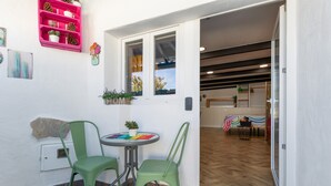 Ein Zimmer mit einer Schiebeglasdoor zum Holzfußbodenbereich, einem kleinen runden Tisch mit Stühlen und einem rosa Regal mit Dekoration.
