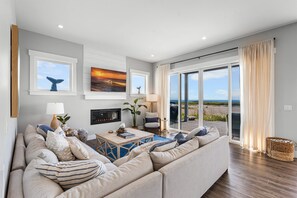 A modern living room with a large sofa, a fireplace, and a view of the beach. - Oceanfront 5BR | Hot Tub, Game Room & Kids Bunk Room | Steps to Pacific (Westport)