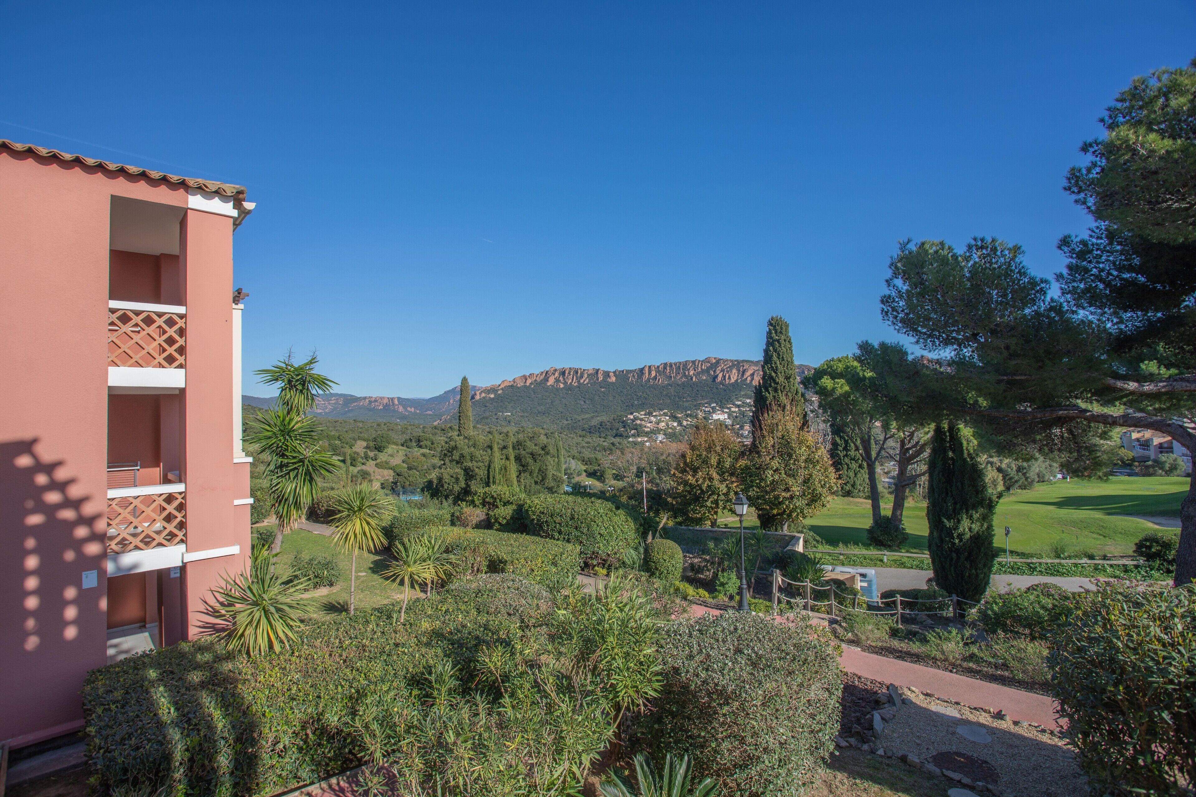 Un bâtiment doté de balcons, un jardin avec différentes espèces de plantes et, en arrière-plan, un paysage montagneux.