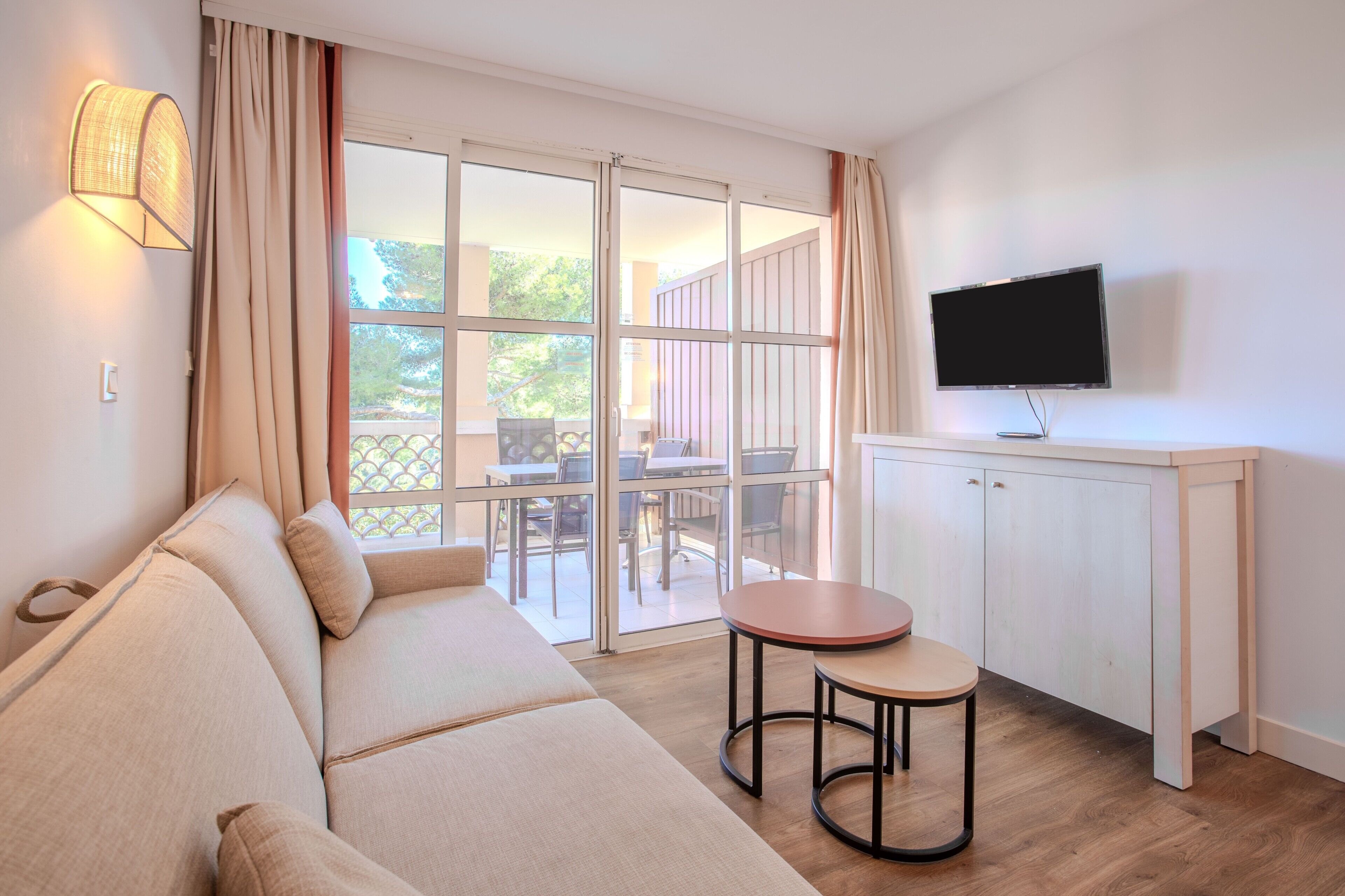 A modern living room with a sofa, a small table, a TV, and a sliding glass door leading to an outdoor area.