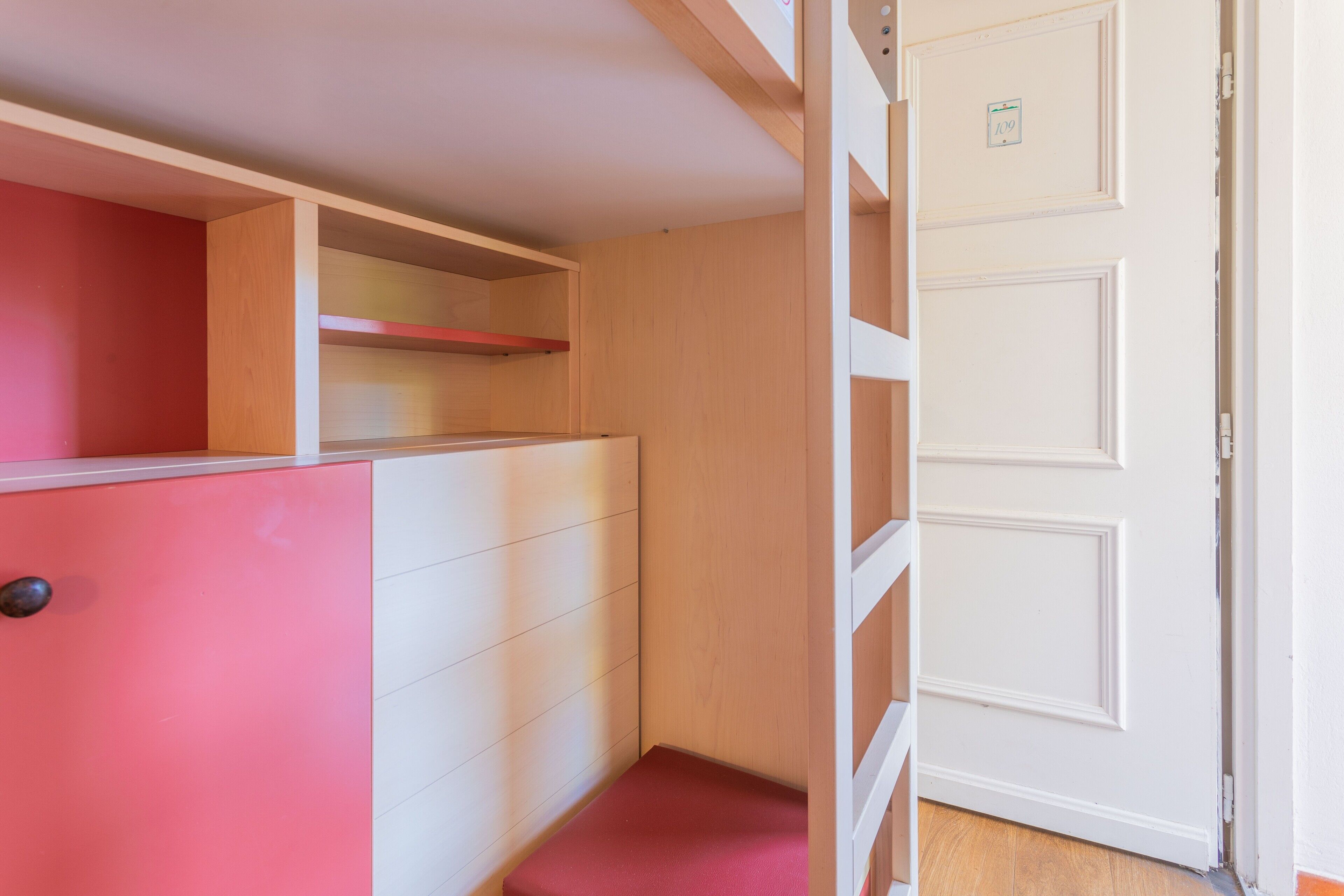 Una habitación con un armario rosa, una puerta de madera y una pared blanca.