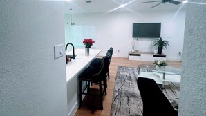 Een moderne keuken met een wit aanrecht, zwarte stoelen en een vaas met rode bloemen.