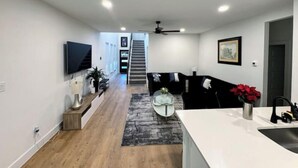Een moderne keuken met een wit aanrecht en een spoelbak, een zwarte bank en een trap naar een ander niveau.