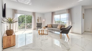 A spacious living room with a sofa, chairs, a TV, and a balcony with a view. - Villa 'Costacabana -  La Luna' with Sea View, Private Pool and Wi-Fi (Lloret de Mar)
